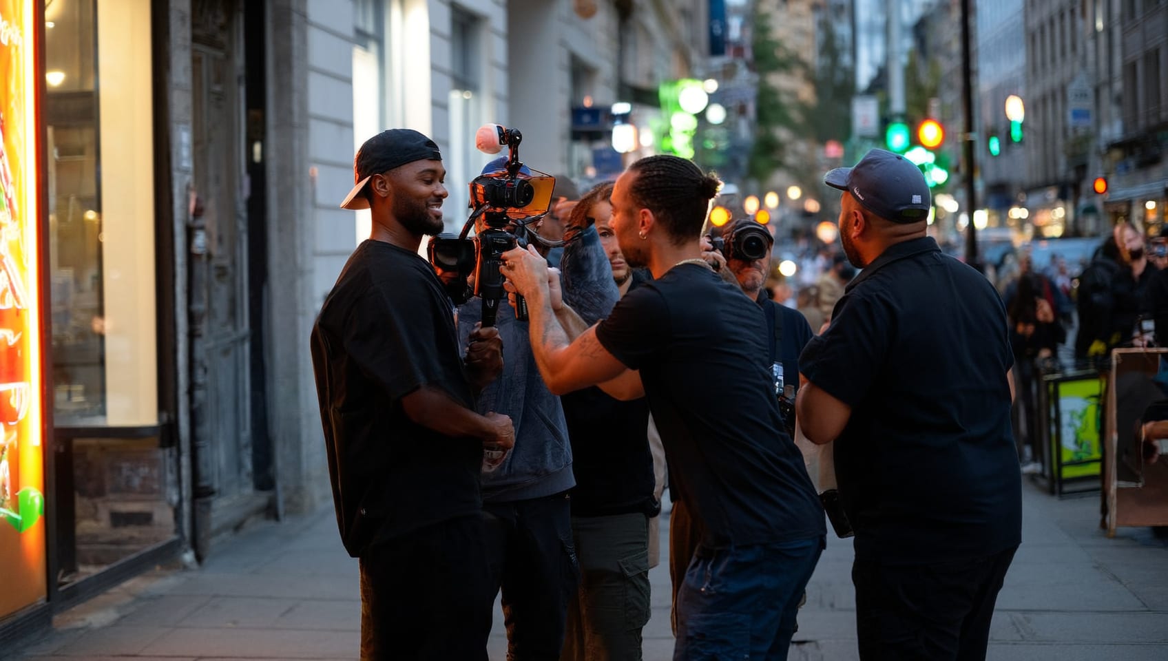 A branded content crew filming a presenter on a city street at dusk with a gimbal camera and LED light