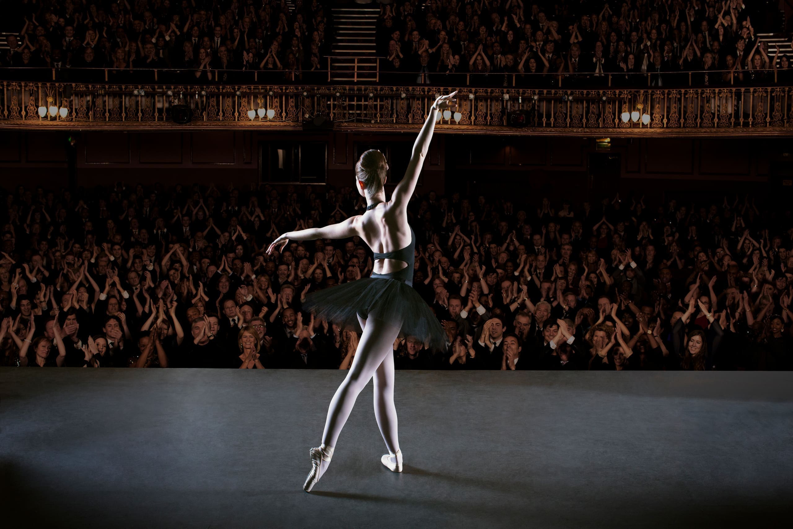 A dancer takes a bow center stage as a full theater audience rises in applause