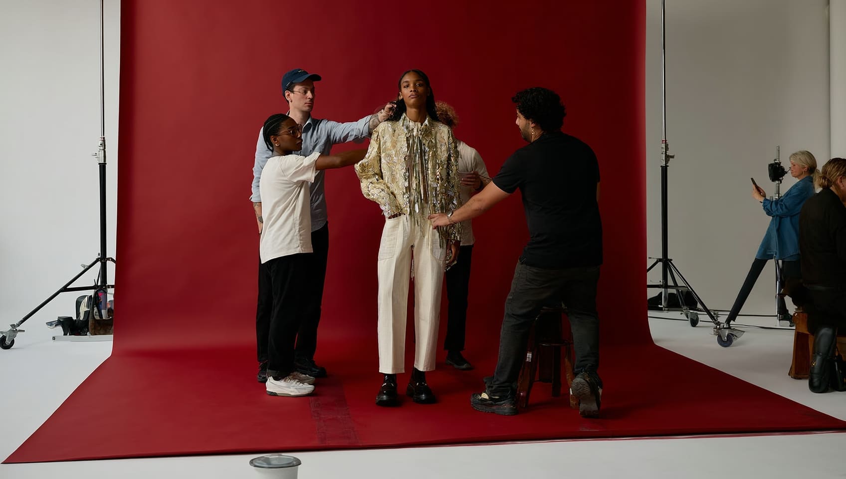 Stylists dressing a model against a red backdrop on a studio set during a photo shoot